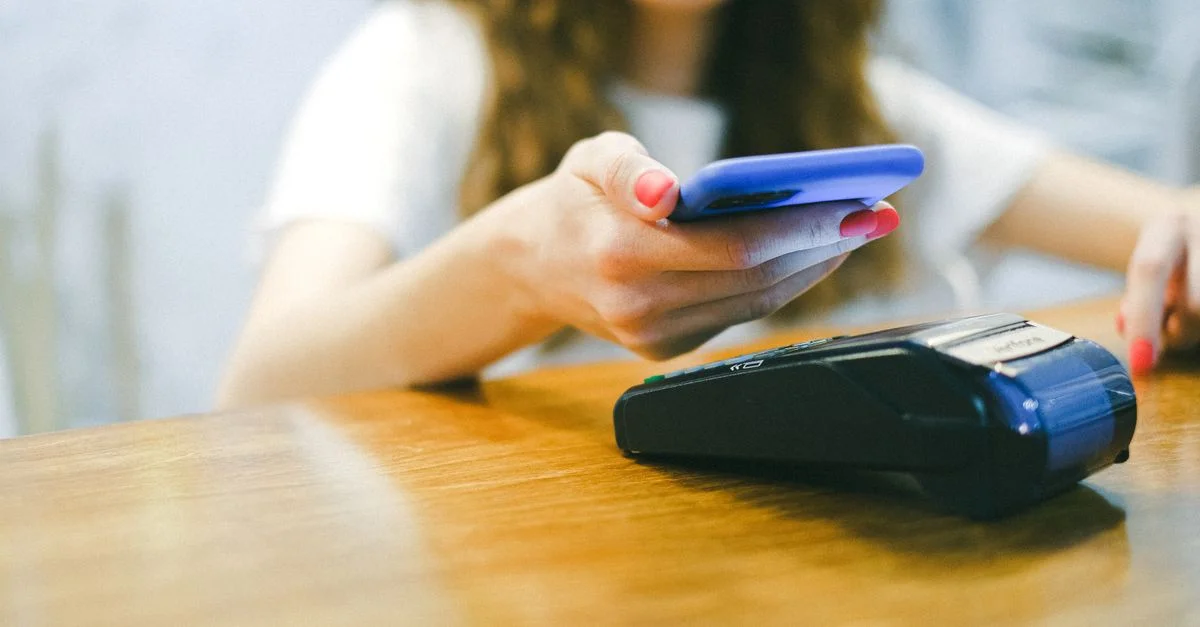 Une femme effectue un paiement sans contact à l'aide de son smartphone à un terminal de paiement.