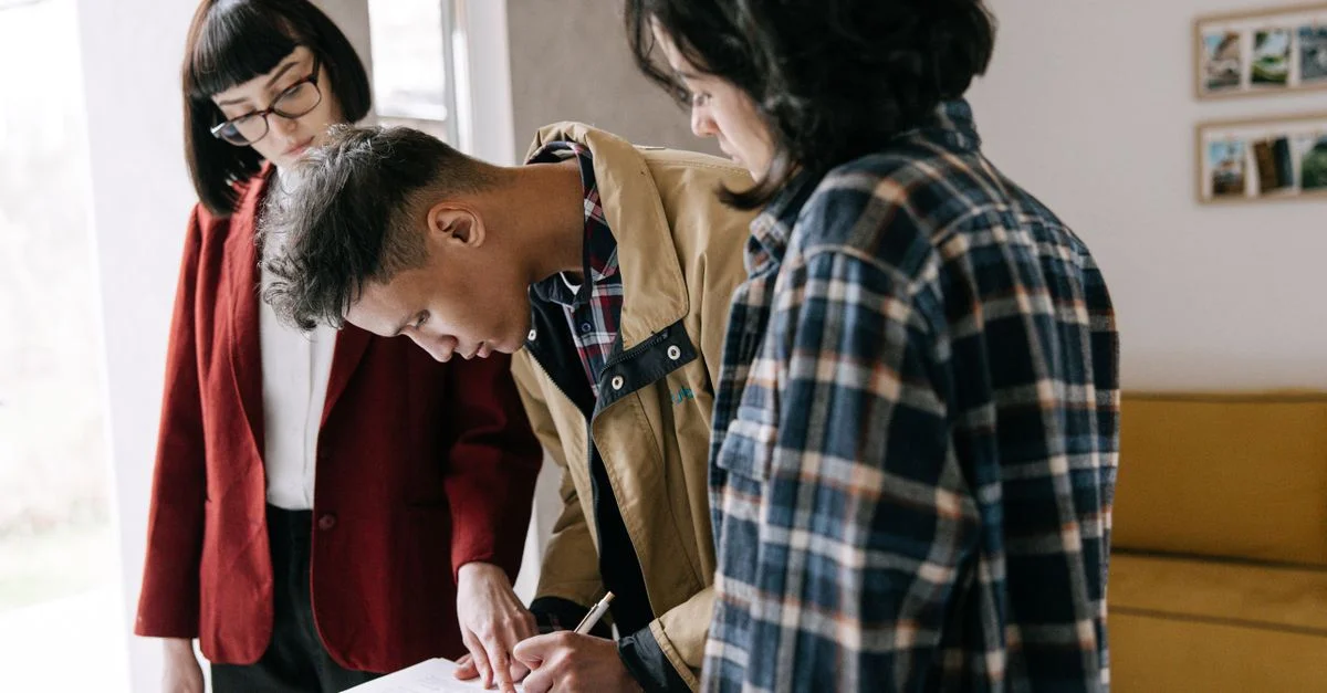 Un jeune couple signe un contrat immobilier avec un agent à l'intérieur.