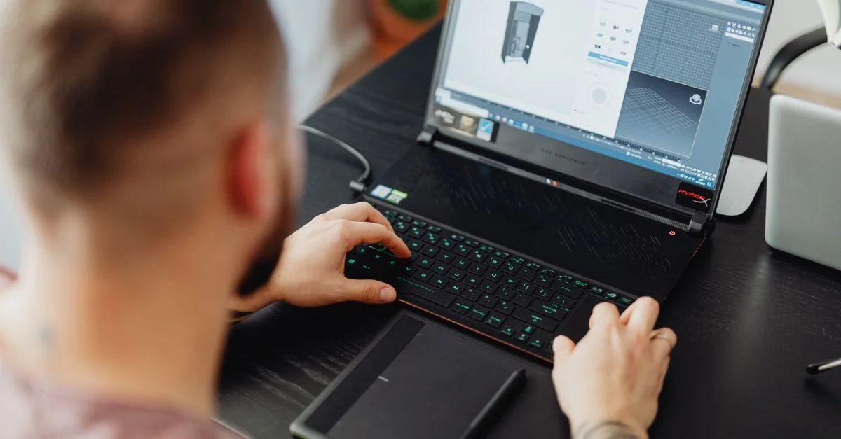 Homme utilisant un ordinateur portable et une tablette pour le design 3D, mettant en avant un environnement de travail numérique moderne.