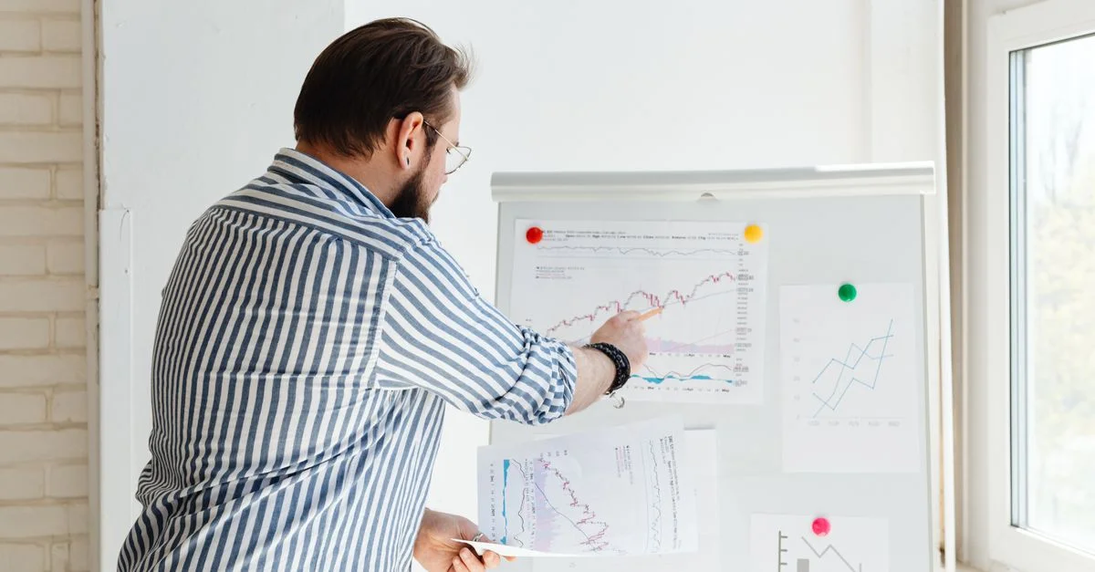 Un homme d'affaires montrant des graphiques financiers sur un tableau blanc, discutant des tendances du marché boursier.