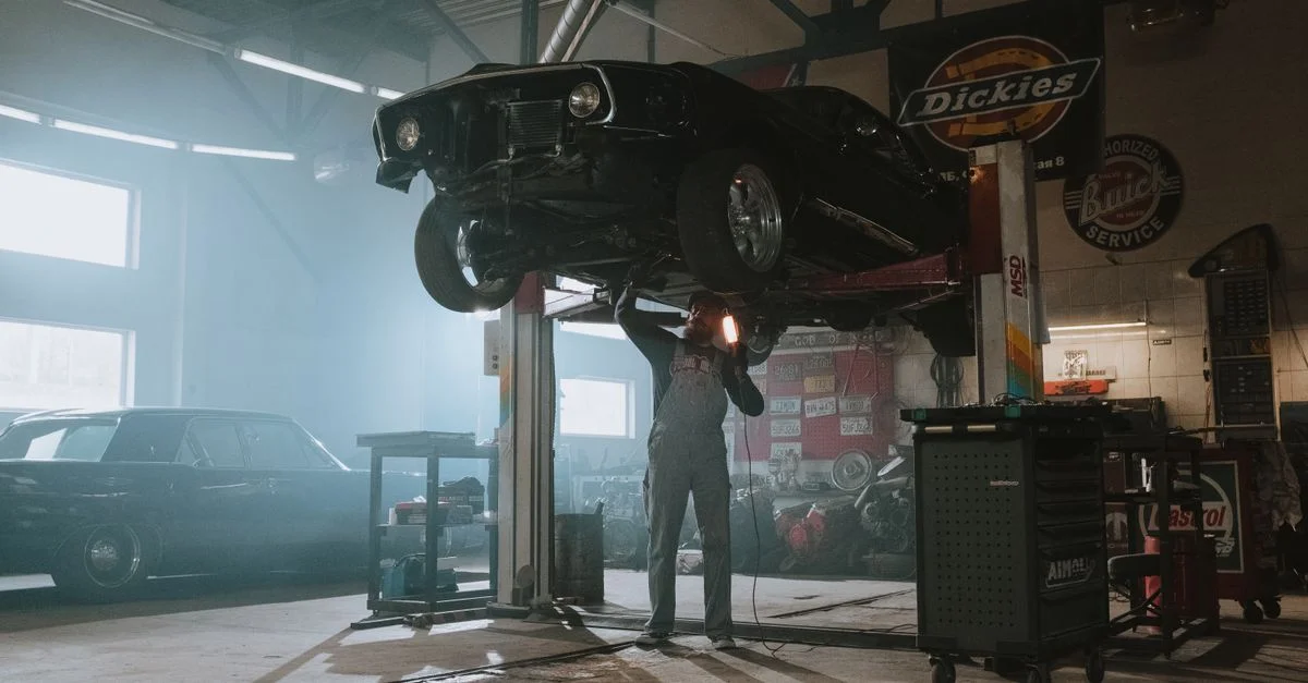 Un mécanicien inspecte une voiture classique soulevée dans un garage automobile à l'aide d'une lampe.