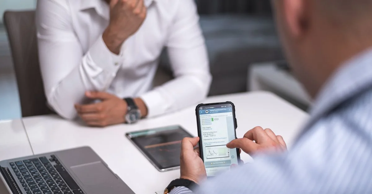 Deux hommes d'affaires dans une salle de réunion utilisant un smartphone et un ordinateur portable pour une discussion professionnelle.