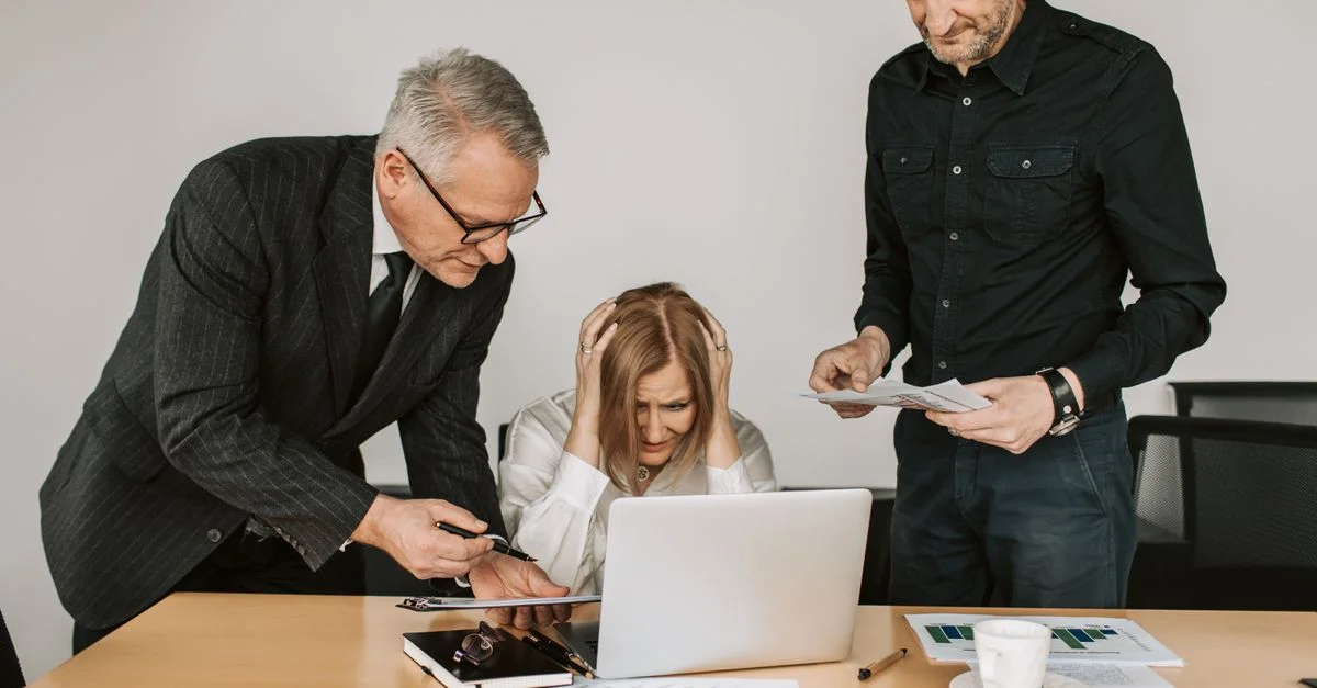 Trois professionnels, dont une personne âgée, lors d'une réunion tendue autour d'un ordinateur portable.