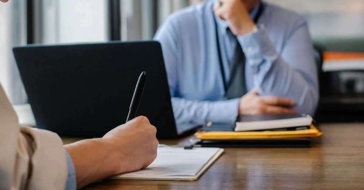 Gros plan sur une interaction lors d'un entretien d'embauche avec des documents et un ordinateur portable dans un bureau.