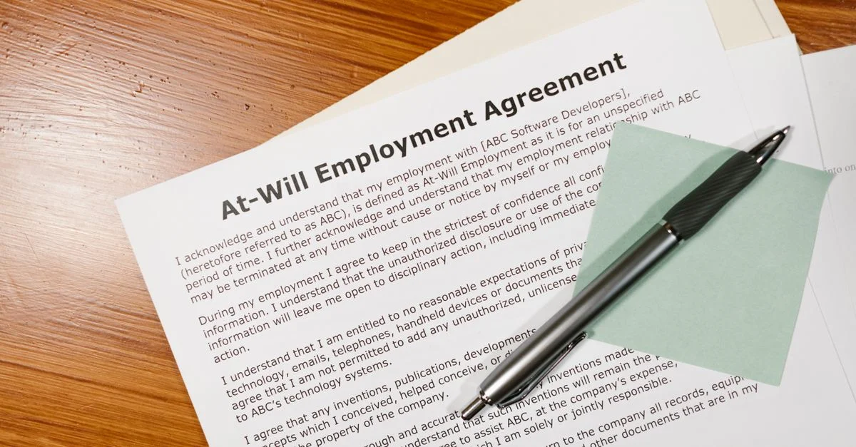 Gros plan sur un contrat de travail à volonté sur un bureau en bois avec un stylo, mettant en avant des concepts juridiques et commerciaux.