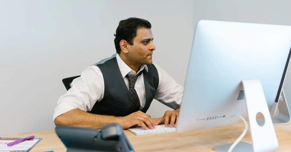 Homme professionnel en tenue de bureau tapant sur un ordinateur à un bureau moderne.