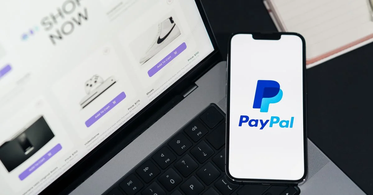 Smartphone affichant le logo PayPal à côté d'un ordinateur portable avec un site d'achat en ligne ouvert.