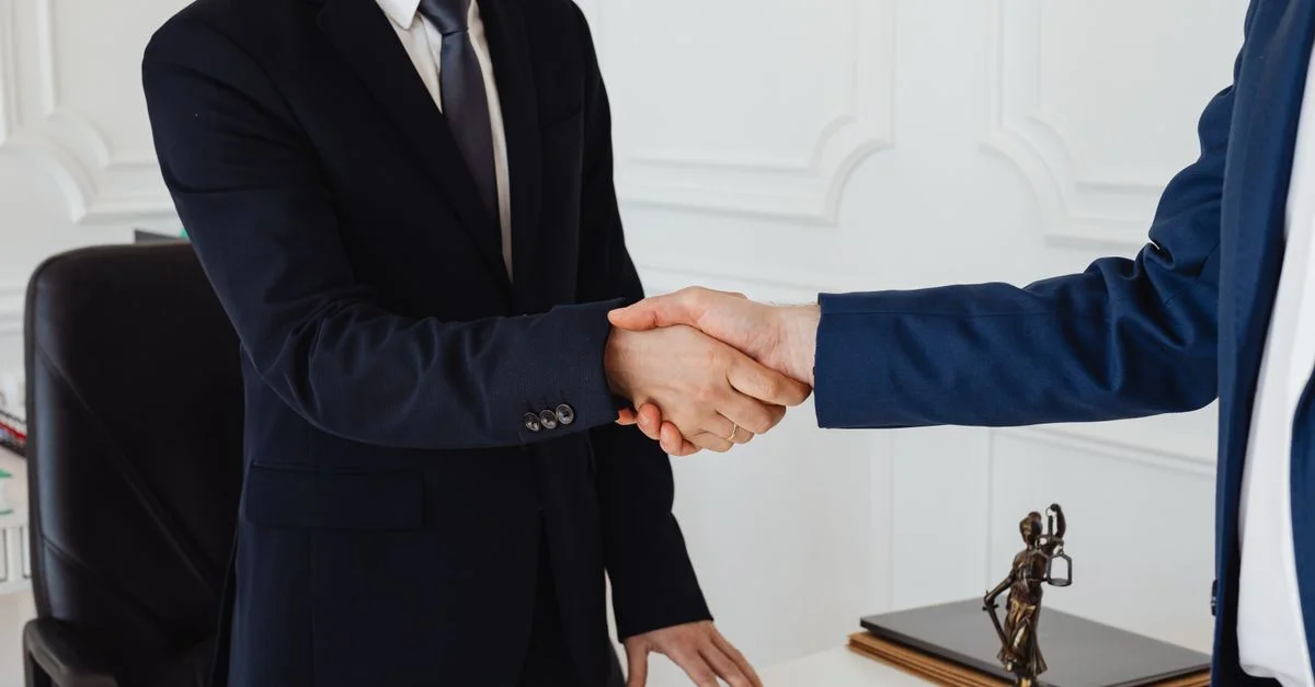 Deux hommes en costume se serrant la main dans un environnement de bureau formel symbolisant un accord.