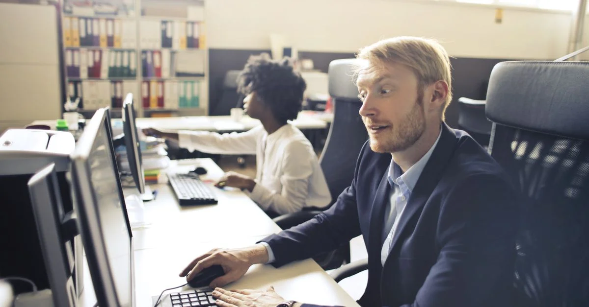 Collègues engagés collaborant dans un bureau moderne, travaillant sur leurs ordinateurs tout en discutant des détails du projet.