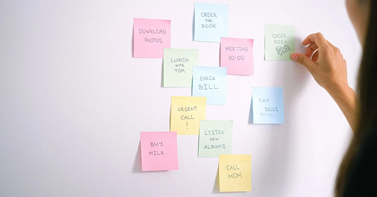 Une collection de post-it colorés sur un mur blanc avec une main qui les organise.