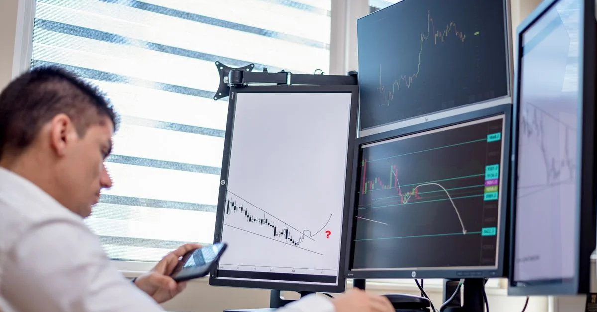 Un trader analyse des données financières sur plusieurs écrans d'ordinateur dans un cadre de bureau.