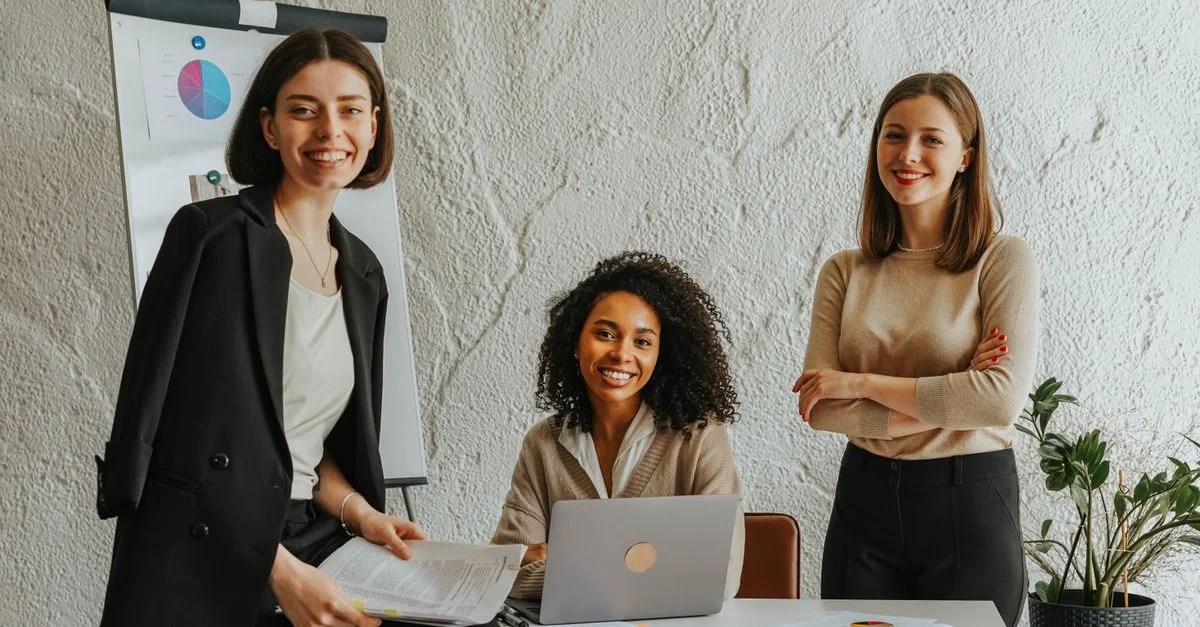 Trois femmes d'affaires se réunissant autour d'une table, utilisant un ordinateur portable et présentant des graphiques dans un bureau moderne.